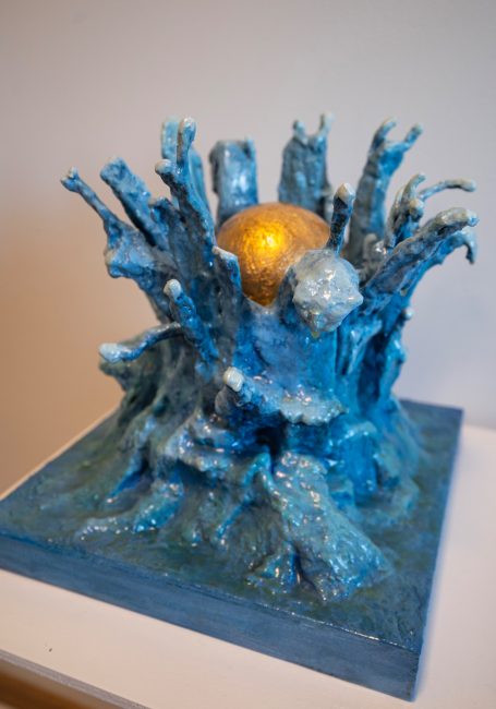 Escultura abstracta en azul con una esfera dorada en la parte superior.