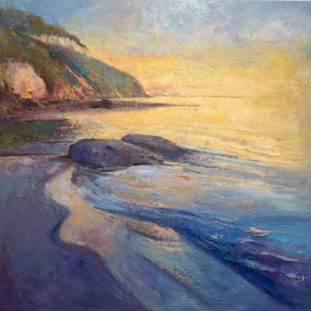 Atardecer en la playa, con rocas y reflejos dorados en el agua.