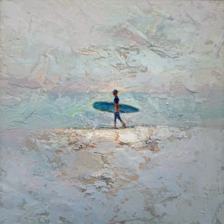 Persona caminando sobre la playa con una tabla de surf bajo un cielo claro.