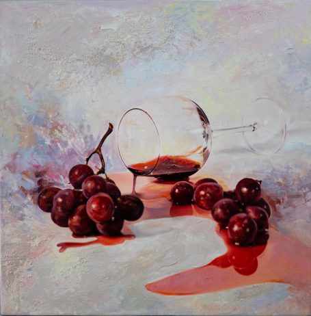 Vino derramado junto a uvas moradas y una copa caída sobre una superficie clara.